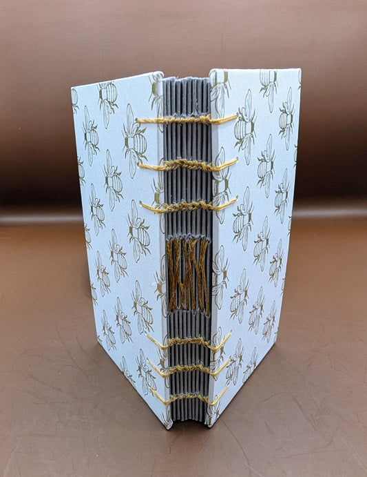 Whimsical handmade 3x5" mini sketchbook with a cute honey bee print. Includes 80 pages of gray cardstock, perfect for sketching, white markers, & journaling. Shown standing up.