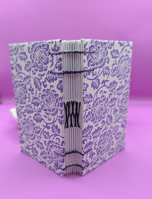 Handmade mini sketchbook featuring purple embossed flowers (Italian paper) and a decorative purple French Stitch. Shown the sketchbook standing up, the stitches are notably visible.