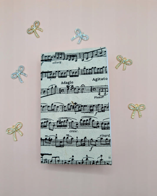 Handmade mini sketchbook featuring purple melody notes pattern on a fine paper from Nepal and a decorative purple French Stitch. Shown sketchbook laying down.