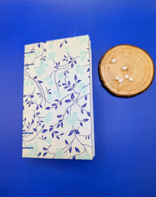 Handmade mini sketchbook featuring turquoise flowers and blue leaves decorative paper from Italy with blue wax thread on an exposed French stitch binding, shown laying showing front cover.