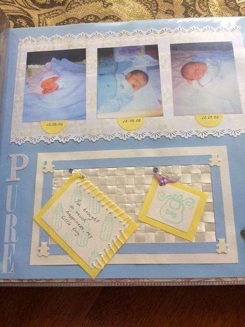 Handcrafted 12x12 baby boy scrapbook page in shades of blue with three rectangular photo frames at the top, decorative lace trim, and a center woven panel with a yellow keepsake note.