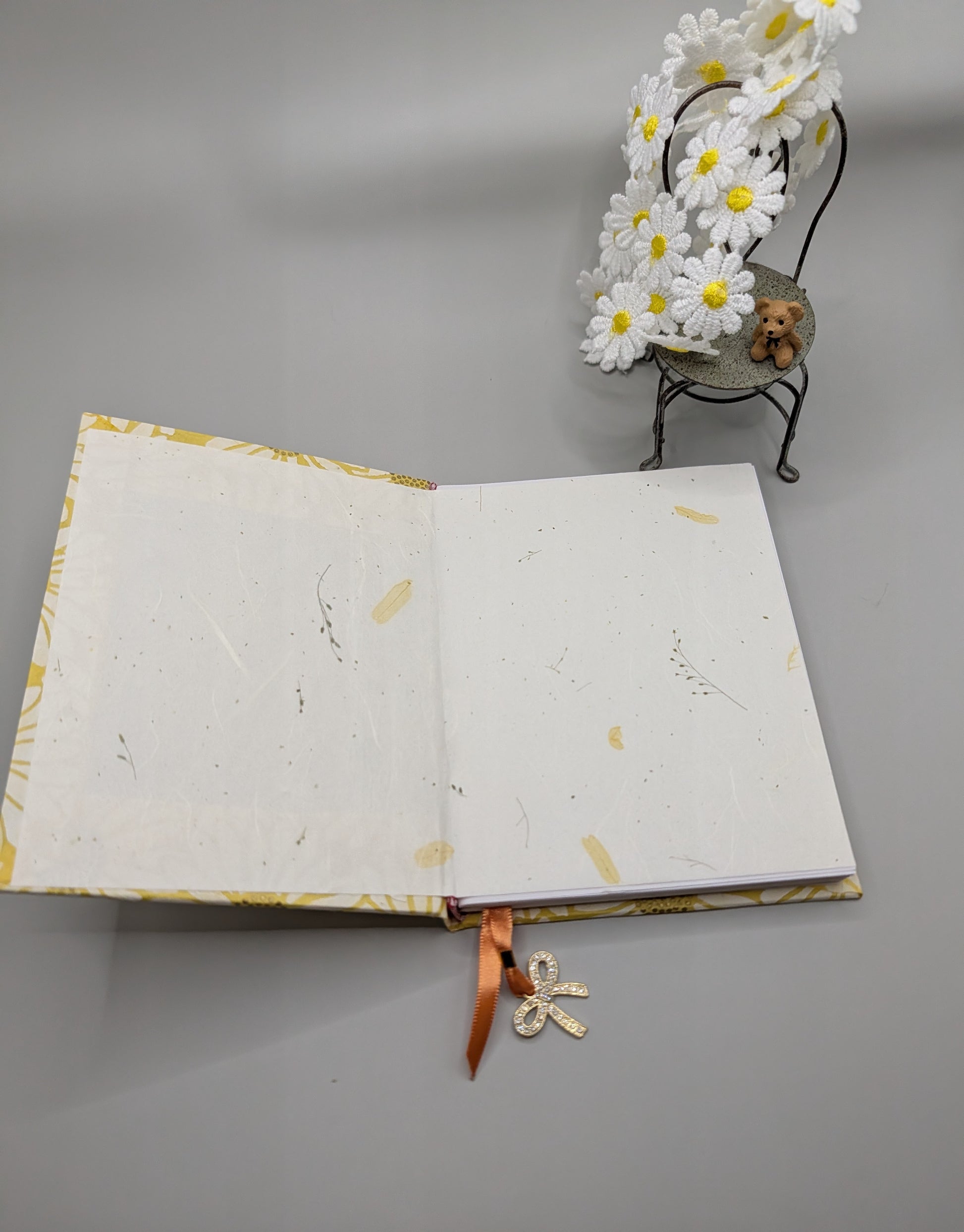 Artisan handmade hardcover journal featuring yellow Nepal daisy paper cover and orange ribbon charm. Showing the inside of journal, feauturing scrapbooking paper.