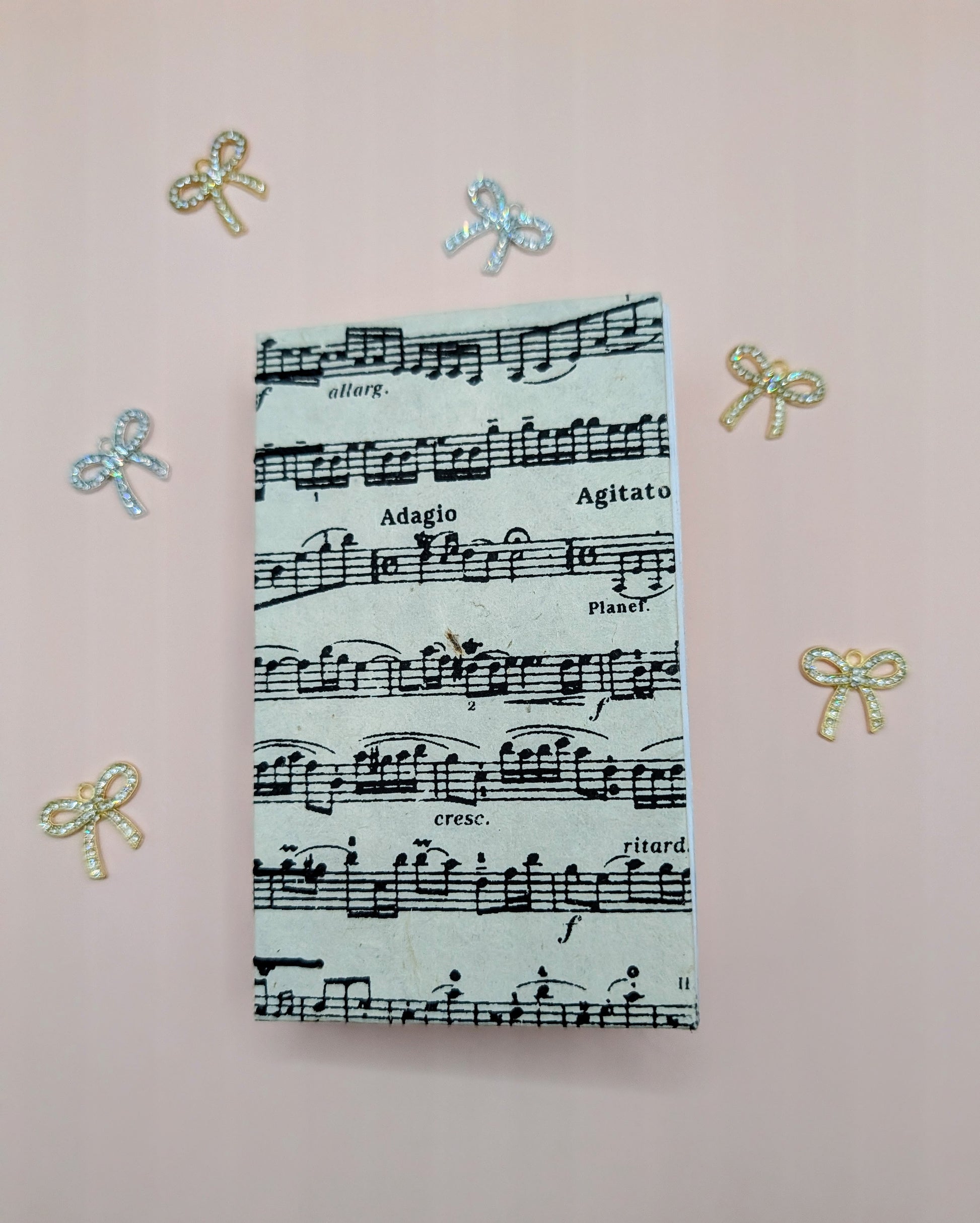 Handmade mini sketchbook featuring purple melody notes pattern on a fine paper from Nepal and a decorative purple French Stitch. Shown sketchbook laying down.