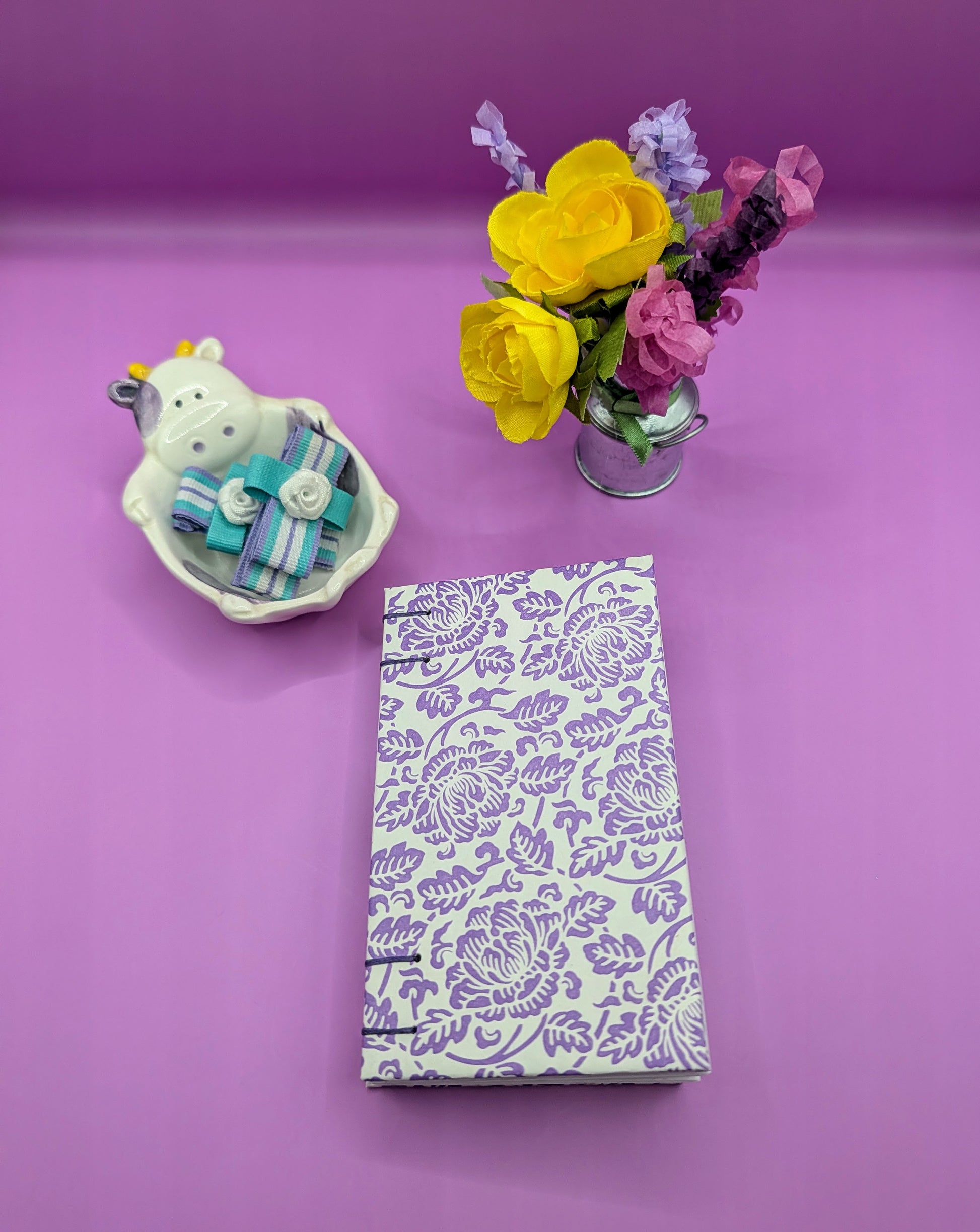 Handmade mini sketchbook featuring purple embossed flowers (Italian paper) and a decorative purple French Stitch. Shown front of the sketchbook.