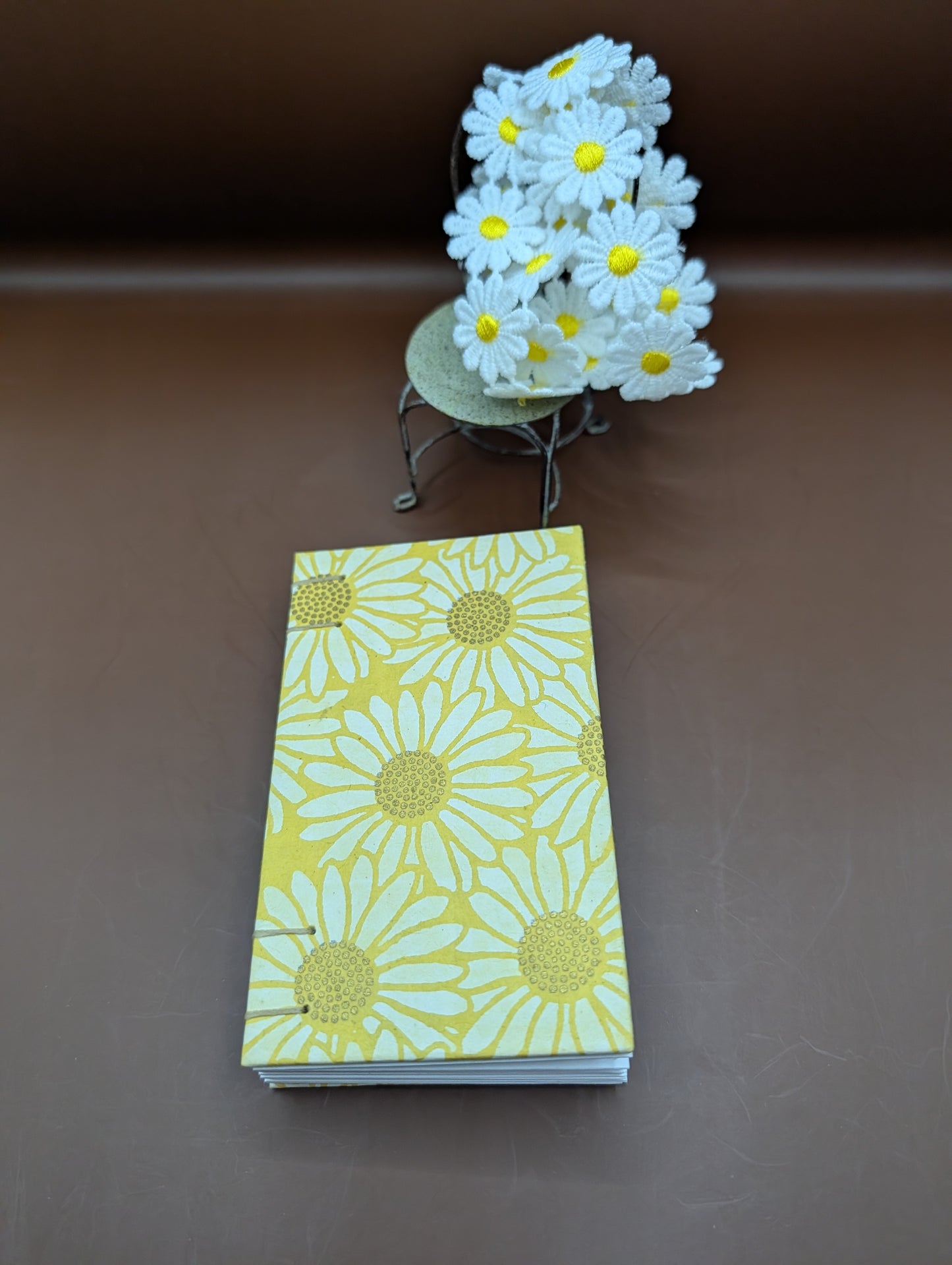 Pocket-sized 3x5" handmade daisies on yellow background pattern. Features 96 pages of cold press paper gorgeous gold French stitch binding, and Nepal paper covers. Shown front cover.